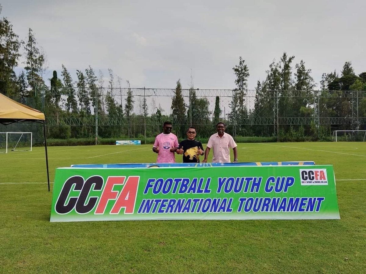 เจ้าหน้าที่การแข่งขันยืนหลังป้าย CCFA Football Youth Cup บนสนาม