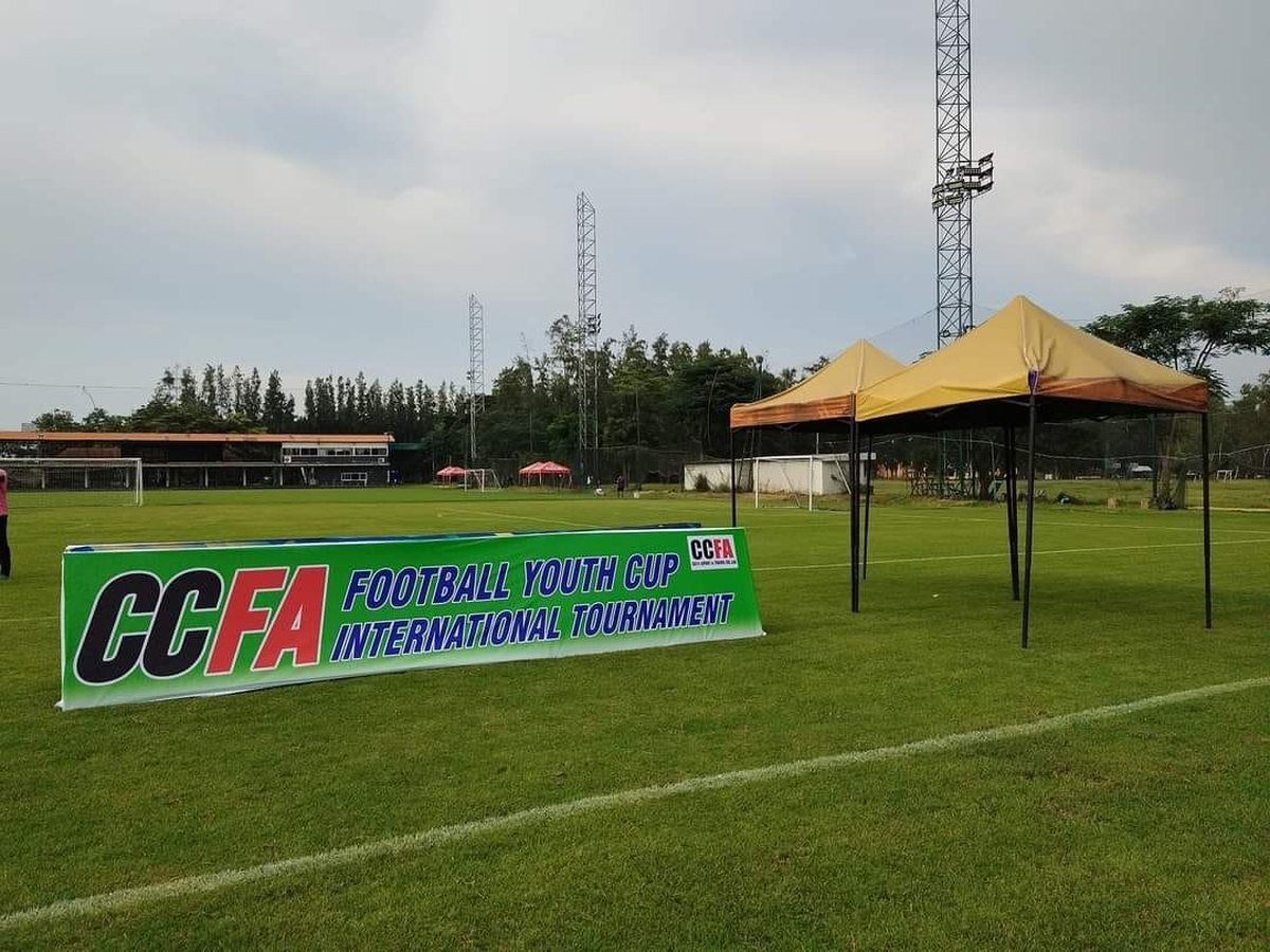 ป้าย CCFA Football Youth Cup บนสนาม มีเต็นท์อยู่ด้านหลัง